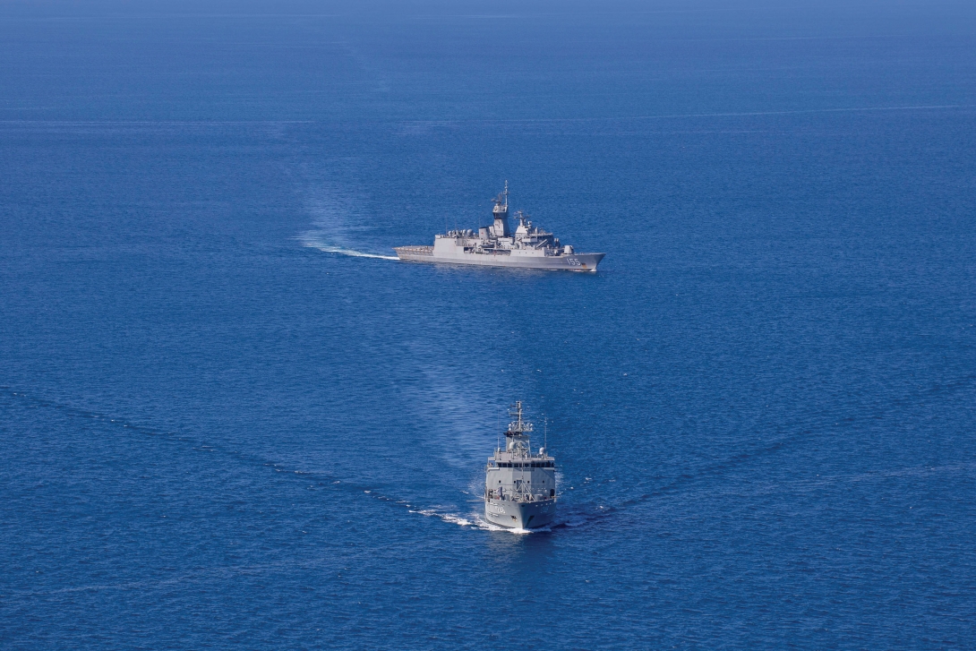 Two navy vessels conducting manoeuvres on the ocean as part of a training exercise. One vessel is moving from the left of the picture to the right whilst the other is moving straight ahead.