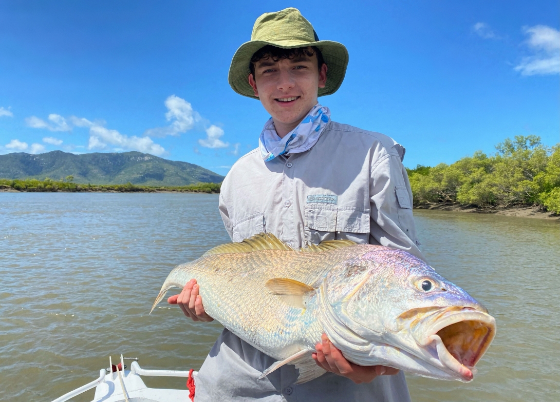 Young fisherman holding a large fish he caught. Mangroves and mountain ranges are in the background. 