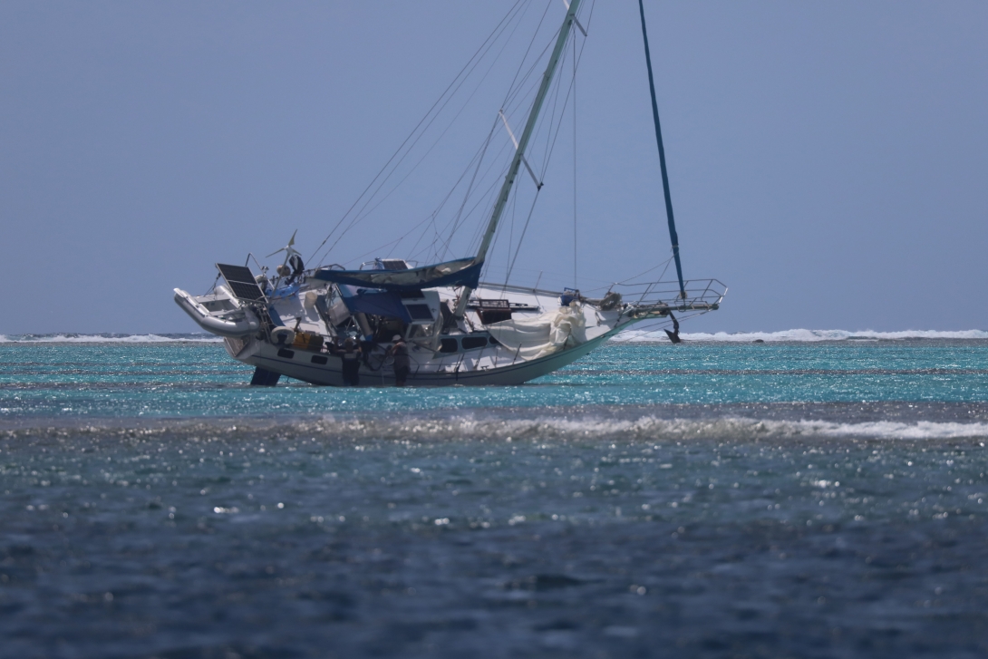 Photo of a recreational vessel grounded on top of a reef. The whole vessel is exposed above the water line. 