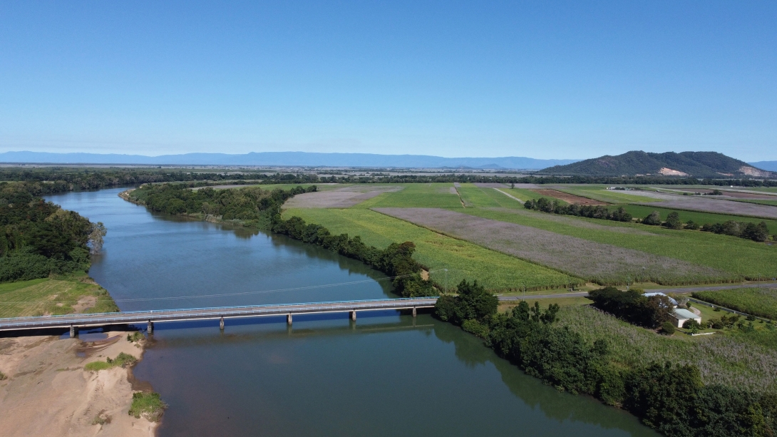 Aerial photo of a bridge crossing a river, with agricultural fields in background.