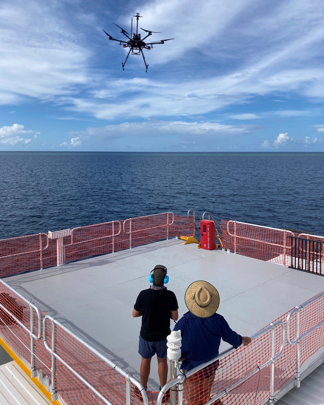 A drone is pictured being operated by two people standing on a platform at sea