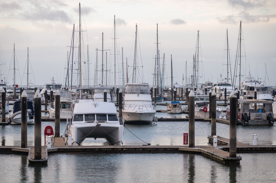 Sailing boats and motor yachts tied up on pontoons in a marina.