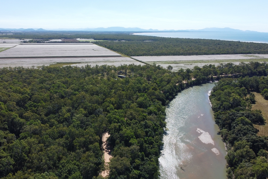 Aerial image showing a river with trees and agricultural landscape, with sea in the background. 