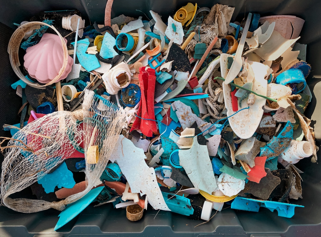 A photo of a collection of brightly coloured plastic pieces that have been collected as part of a marine debris cleanup, including nets, string, bottle lids, plastic toy and many broken fragments.  