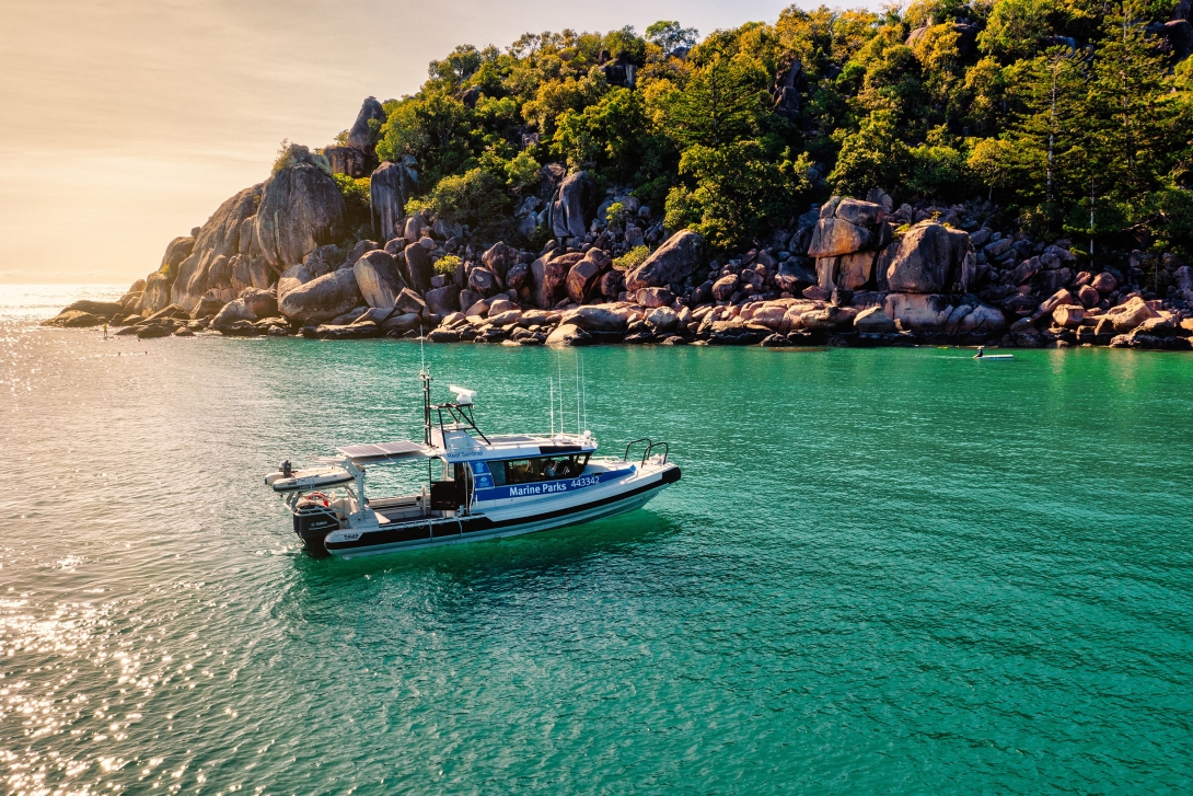 Photo of a Marine Parks rigid hulled boat on the water, with vegetation and boulders in the background. 