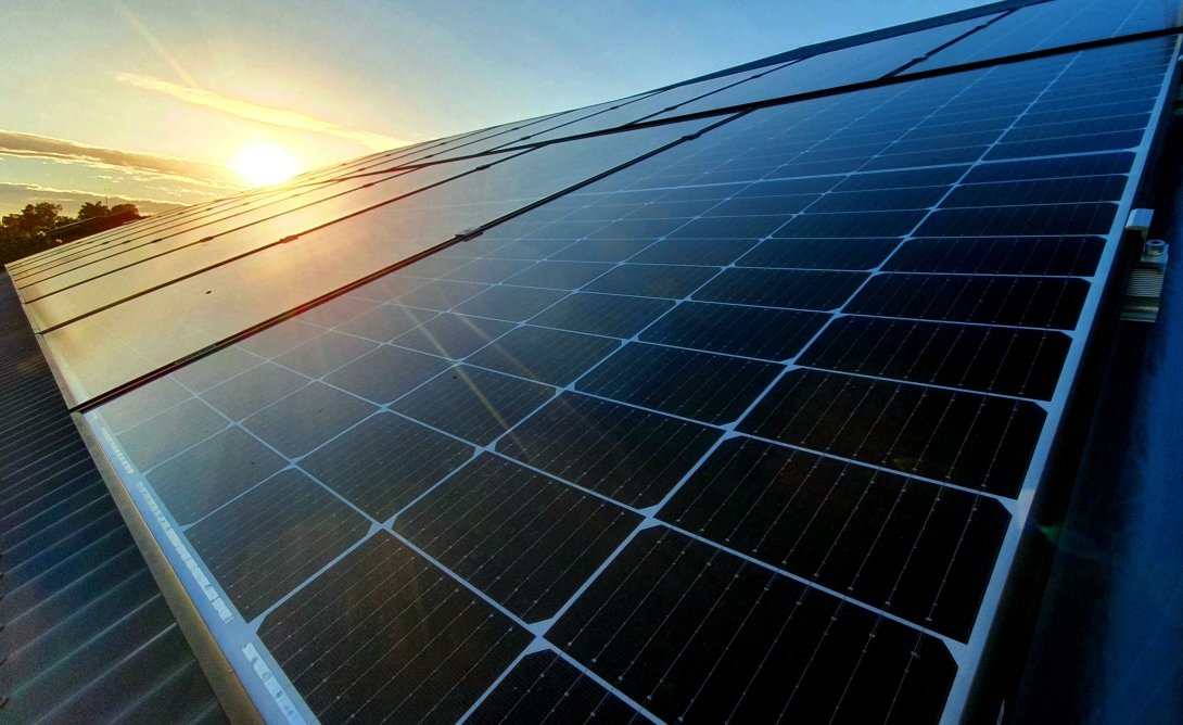 A close-up photograph of rooftop solar panels with the sun shining in the background.