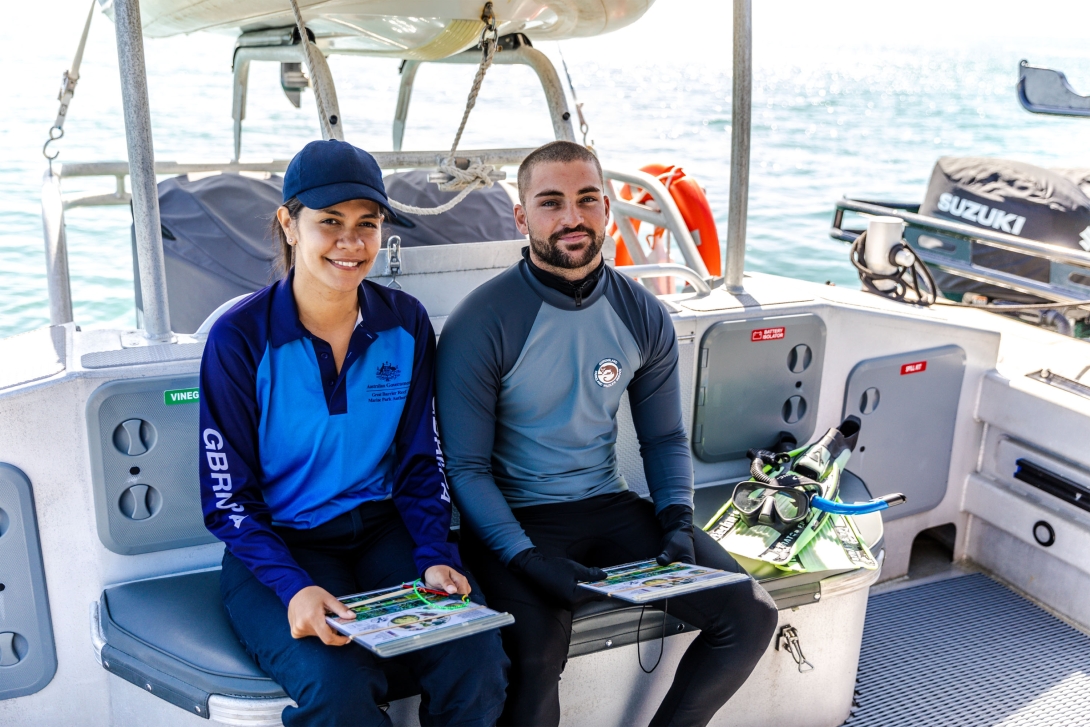 Two people, one from the Reef Authority and another from Queensland Parks and Wildlife Services, sitting in a boat holding survey slates. They are sitting next to some snorkel gear. 