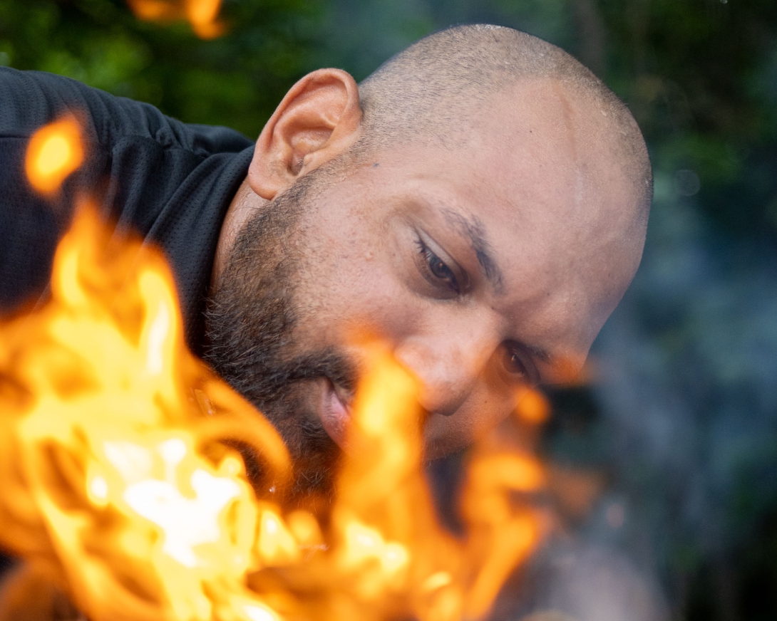 Close-up photo of the traditional Owner observing a small fire in the foreground of the image. 